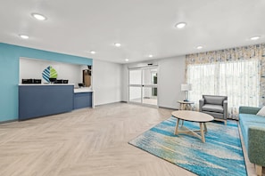 A modern hotel lobby with a reception desk, seating area, and a large window with curtains.