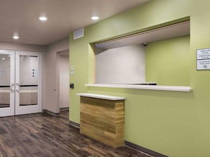 A reception desk with a green wall, a wooden counter, and a sign indicating check-in/out times. - Woodspring Suites St. Joseph (St. Joseph)