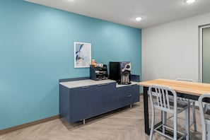 Una stanza con una parete verde acqua, un tavolo in legno, una sedia bianca, un mobile blu scuro e una macchina per il caffè.
