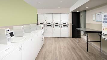 A laundry facility with multiple washing machines and dryers, a table, and a door leading to another room.