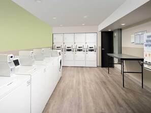A laundry facility with multiple washing machines and dryers, a table, and a door leading to another room.