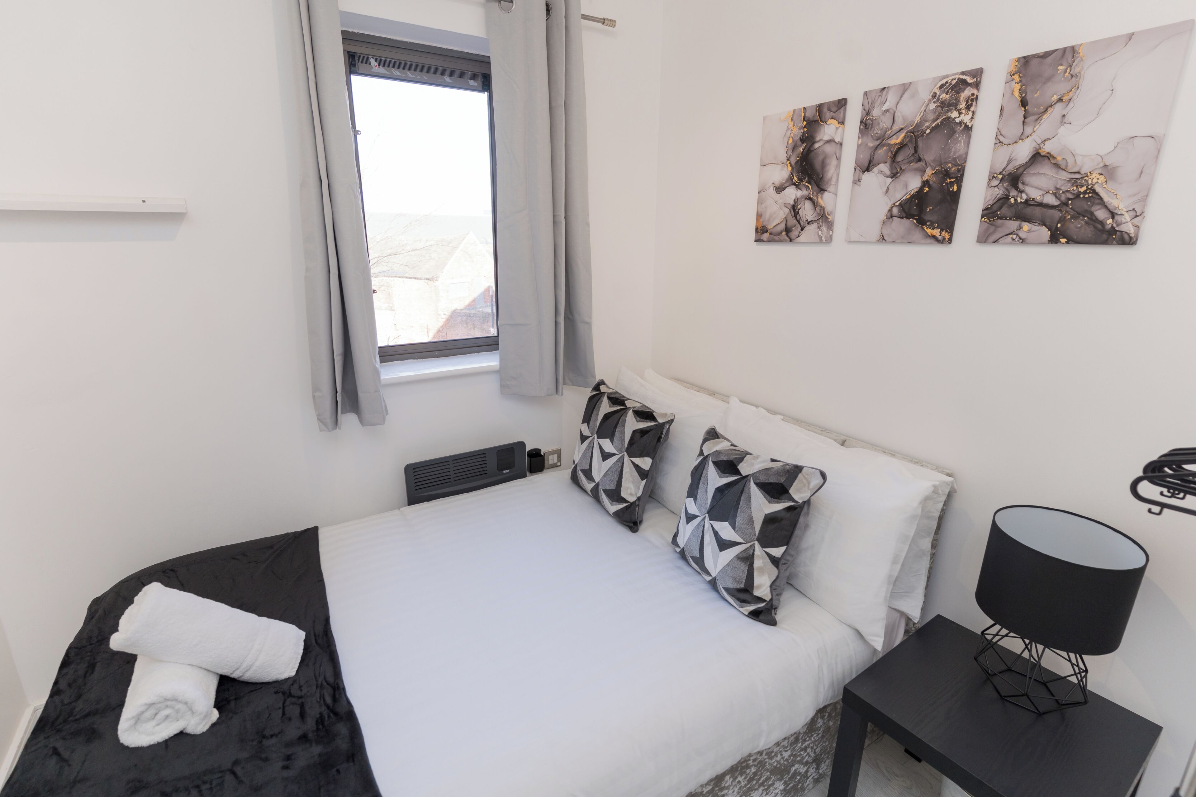 A hotel room with a bed, a bedside table with a lamp, and a window with curtains.