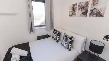 A hotel room with a bed, a bedside table with a lamp, and a window with curtains.