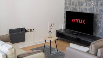 A modern living room with a flat-screen TV displaying 'NETFLIX' in red letters, a small side table with a vase, and a grey patterned wall.