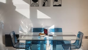 Moderni ruokailutila, jossa on lasipöytä ja siniset tuolit, pieni lautanen ruokaa ja seinätaidetta.