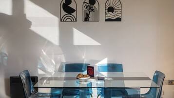 A modern dining area with a glass table and blue chairs, a small plate with food, and wall art.