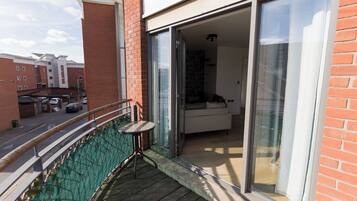A balcony with a table and chairs, a sliding glass door leading to a living area, and a view of the street and other buildings.