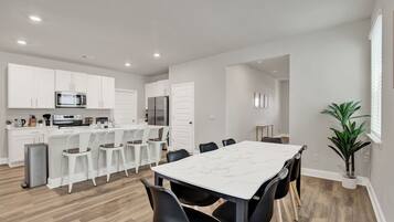 A modern kitchen with white cabinets, a marble countertop, and a dining area with a white table and black chairs.