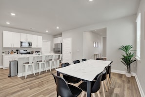 Une cuisine moderne avec des meubles blancs, un plan de travail en marbre et un coin repas comprenant une table blanche et des chaises noires.