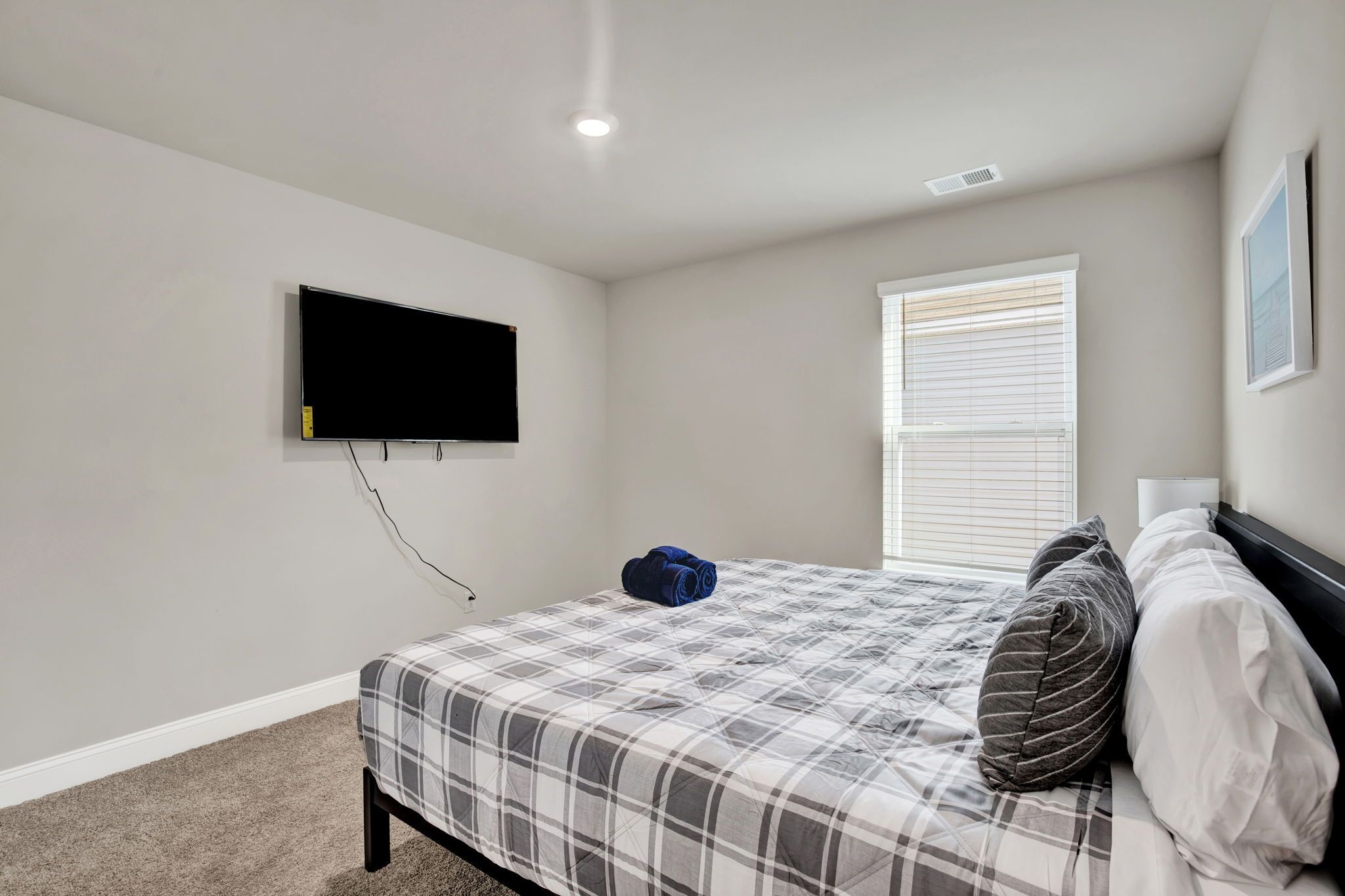 Une chambre à coucher comprenant un lit, un téléviseur à écran plat fixé au mur, une fenêtre avec des stores et un sol recouvert de moquette.