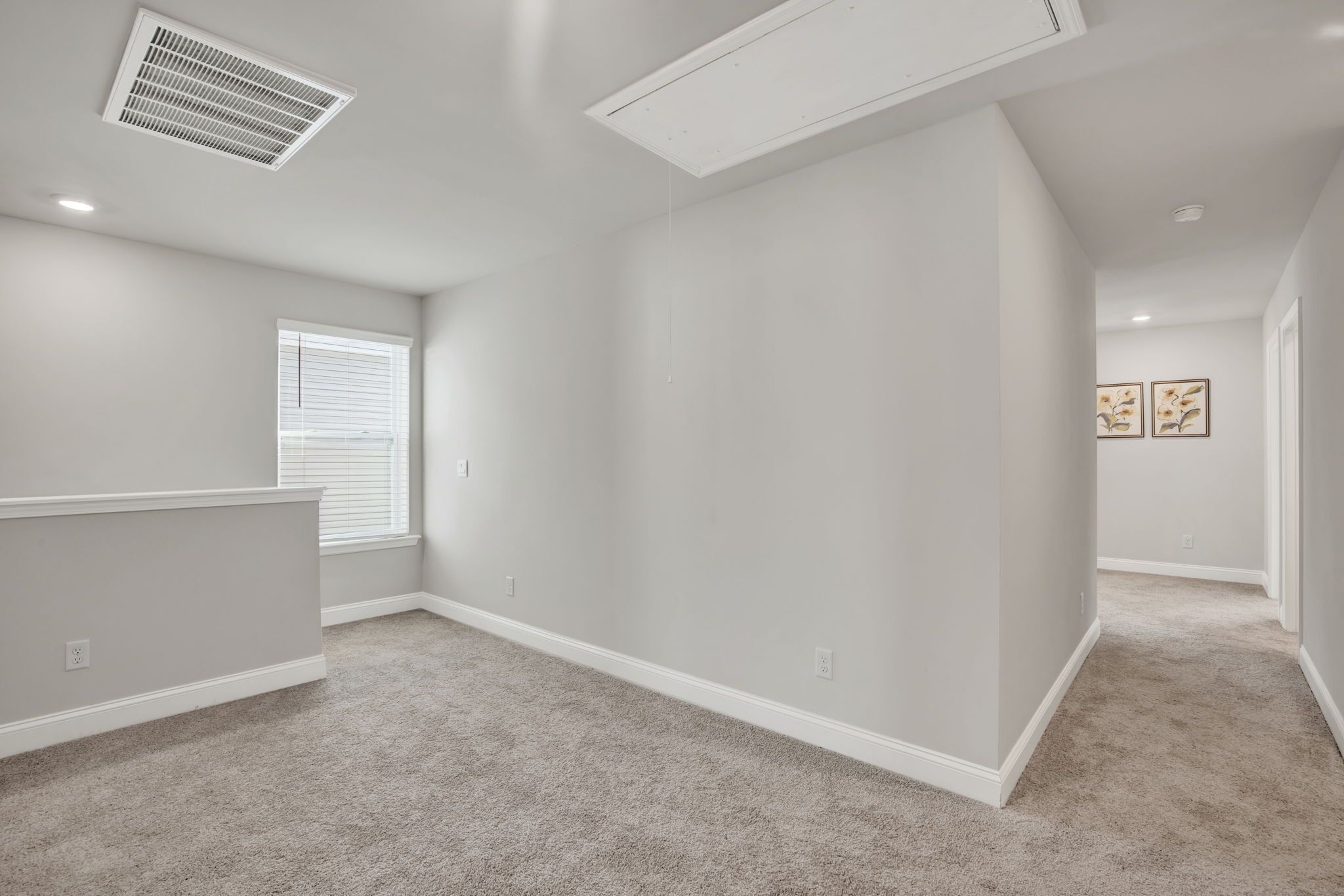 Un'ampia stanza con soffitto spiovente, una grande finestra con tende e pavimento rivestito di moquette.