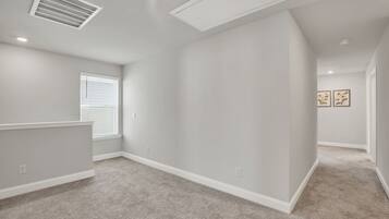Un'ampia stanza con soffitto spiovente, una grande finestra con tende e pavimento rivestito di moquette.
