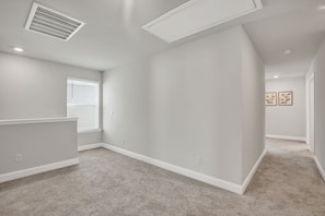 Una habitación amplia con techo inclinado, un ventanal con persianas y suelo alfombrado.