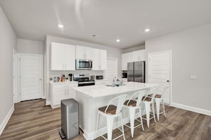 Una cocina moderna con armarios blancos, electrodomésticos de acero inoxidable y una isla central con taburetes de bar.