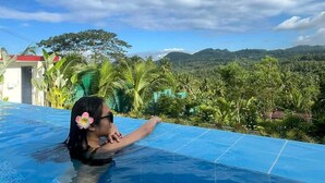 Una persona en una piscina con vistas a un paisaje montañoso y vegetación tropical.