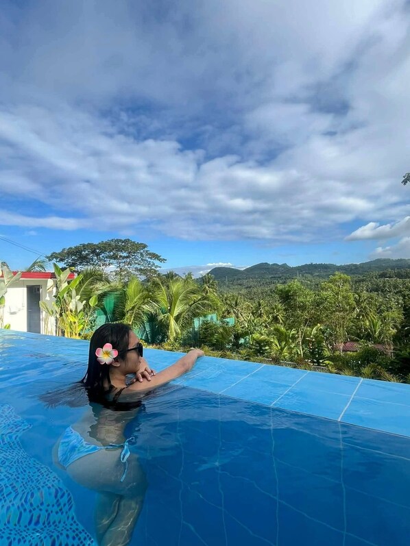 A person in a swimming pool with a view of a mountainous landscape and tropical vegetation.