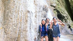 Una cascada con tres personas posando frente a ella.