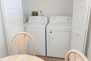 A laundry room with two white washing machines, a wooden chair, and a small picture frame on the wall. - 3BR Pool Home in Kissimmee Sleeps 6 (Kissimmee)