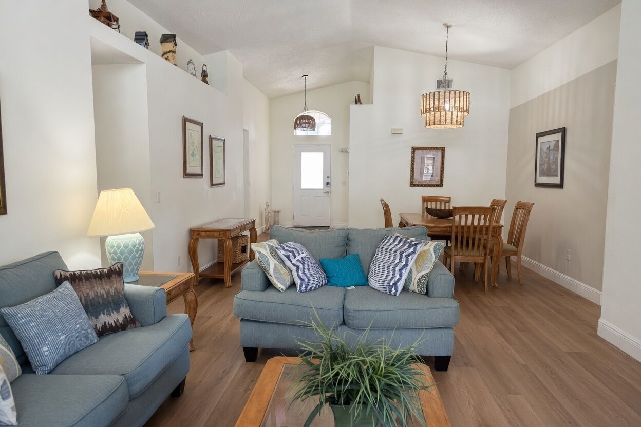 A living room with a sofa, a dining table, chairs, a lamp, and a hanging light fixture.