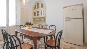 Ein Essbereich mit einem Holztisch, Stühlen, einer Salatschüssel, einem weißen Kühlschrank und einem Fenster mit Jalousien.