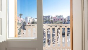 Blick aus einem Fenster mit einem Balkon, auf eine Straße mit parkenden Autos und Gebäuden.