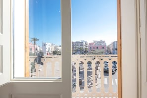 A view from a window with a balcony, overlooking a street with parked cars and buildings. - TD Palazzo Fiume 1 – Heart of Polignano (Polignano a Mare)