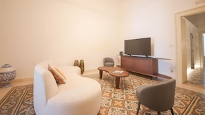 Ein modernes Wohnzimmer mit einer Couch, einem Sessel, einem Couchtisch und einem Flachbildfernseher auf einer Holzkommode.