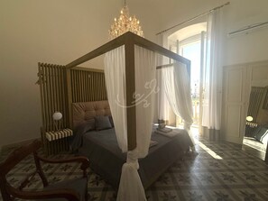 A bedroom with a four-poster bed, a chandelier, a bedside table, and a chair. - TD Palazzo Fiume 1 – Heart of Polignano (Polignano a Mare)