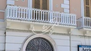 Ein Gebäude mit einem zentralen Eingang, einem Balkon mit weißen Brüstungen und einem Schild, das auf eine Gesellschaft hinweist.