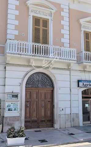 A building with a central entrance, a balcony with white balustrades, and a sign indicating a society. - TD Palazzo Fiume 1 – Heart of Polignano (Polignano a Mare)
