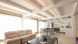 A modern living room with a sofa, a coffee table, and a dining area with chairs. - TD Palazzo Fiume 2 – Above the Square (Polignano a Mare)