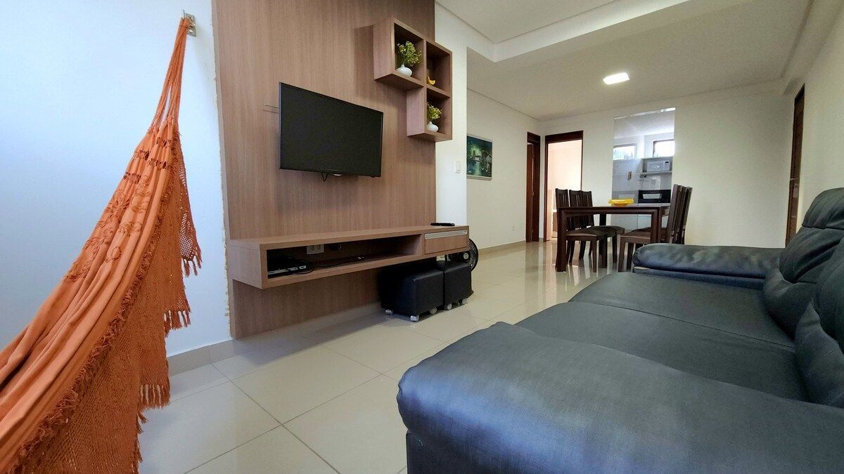 Una sala de estar moderna con un televisor de pantalla plana, un sofá y un área de comedor al fondo.