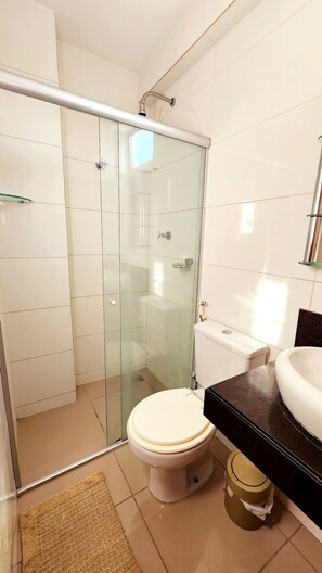 Un baño moderno con cabina de ducha de vidrio, inodoro blanco y lavamanos negro.