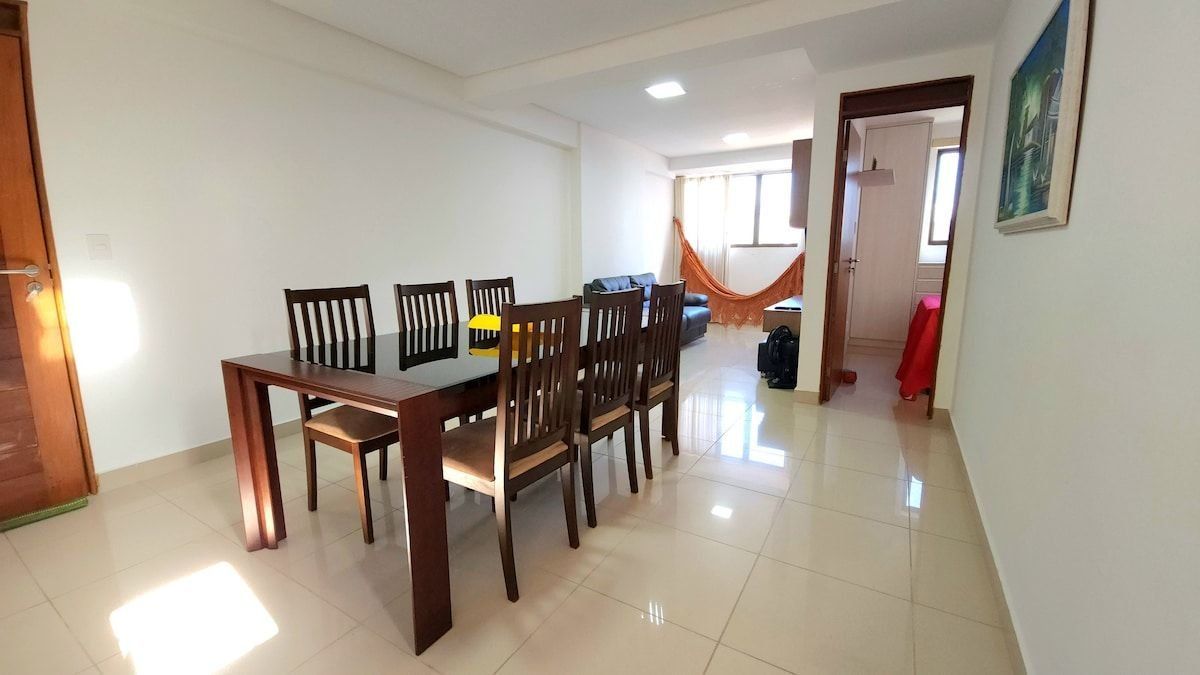 Un comedor con una mesa y sillas de madera, un sofá y una ventana con cortinas.