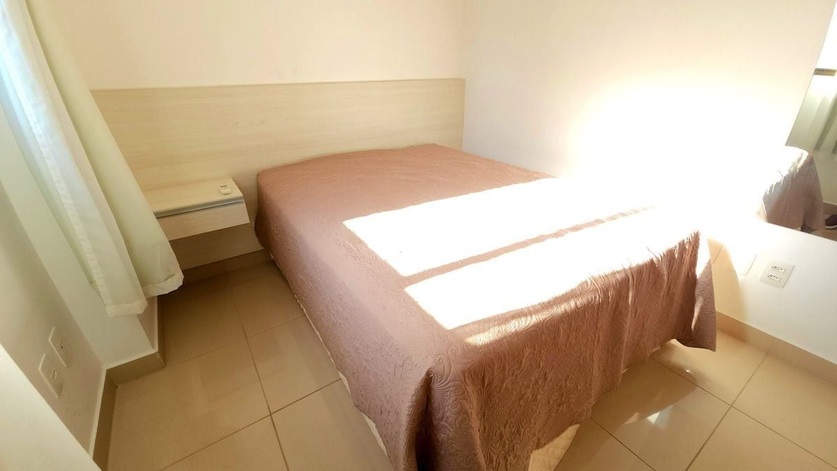 Una habitación con una cama, una mesita de noche, un enchufe y una ventana.