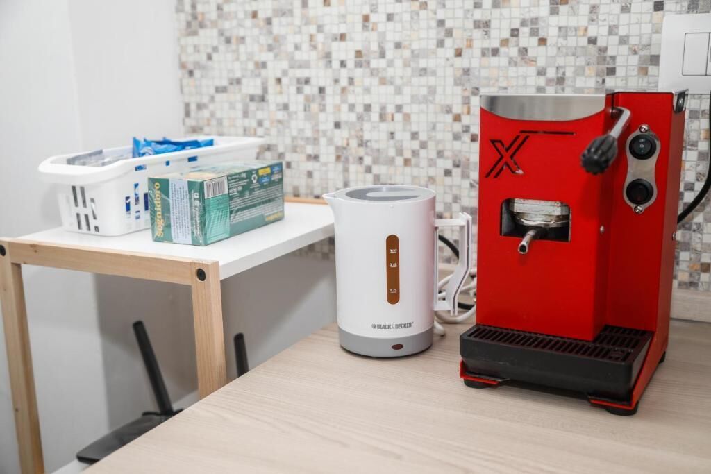 Un coin cuisine comprenant une machine à café, une bouilloire blanche et une boîte de capsules de café, le tout posé sur une table.