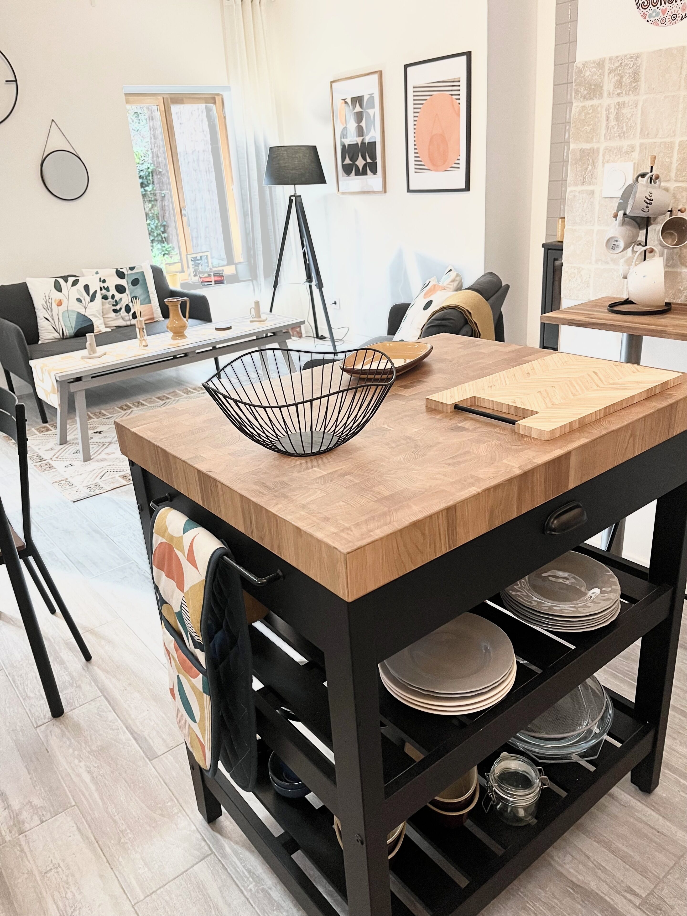 A modern kitchen with a central island, black metal shelving, and a variety of kitchenware.