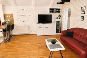 A living room with a red sofa, a coffee table with a plant, a white cabinet with a TV, and a wall clock. - Mrzeżyno holiday home for 5 people (Mrzeżyno)