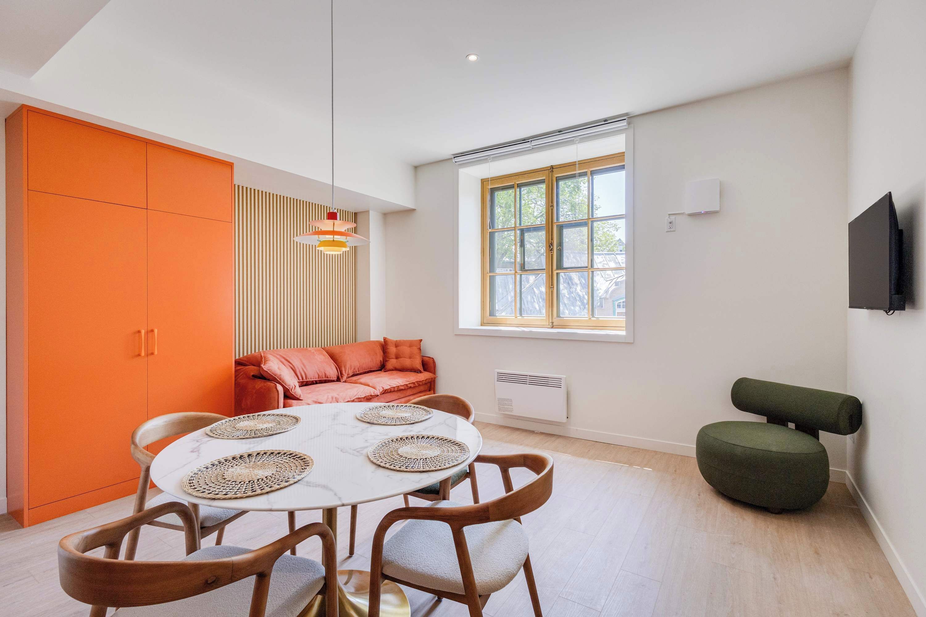 A modern interior with a round dining table, orange cabinetry, a cushioned sofa, and a television mounted on the wall.