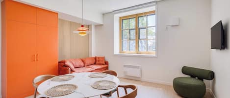 A modern interior with a round dining table, orange cabinetry, a cushioned sofa, and a television mounted on the wall.