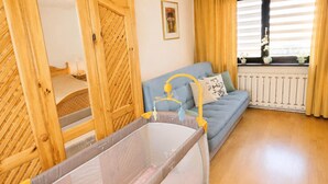 A baby crib with a yellow mobile, a blue sofa with cushions, and a window with curtains. - Holiday home for 6 people Mrzeżyno (Mrzeżyno)