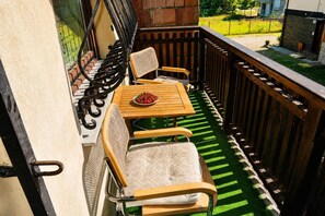 Een balkon met een houten tafel en twee stoelen, een metalen hekwerk en uitzicht op de omgeving.