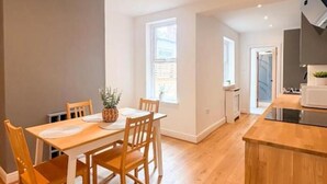 Eine moderne Küche mit Holzboden, einem Essbereich mit Tisch und Stühlen sowie Blick ins Freie durch ein Fenster.