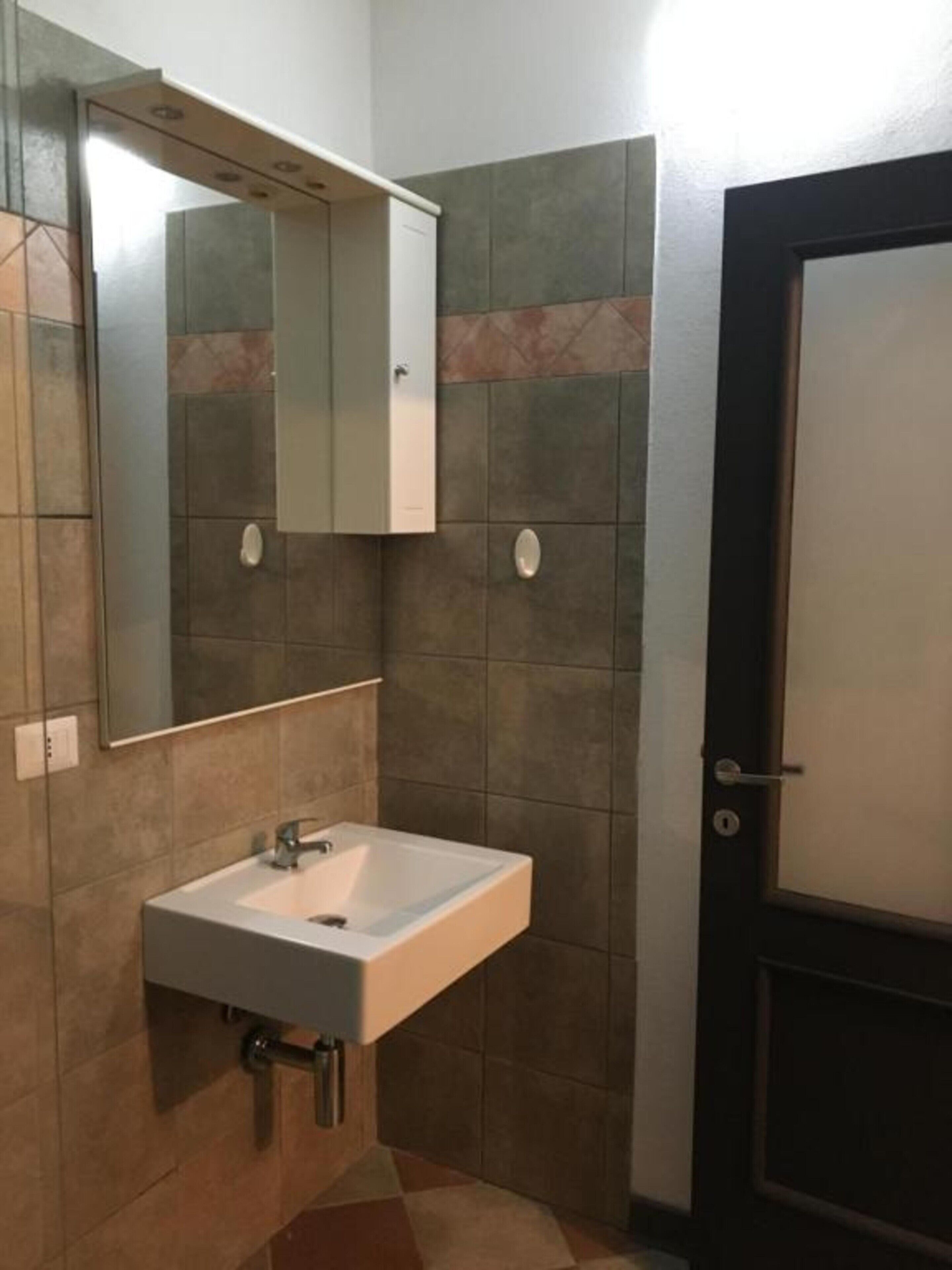 Een badkamer met een wit wastafelmeubel, een spiegel en een deur.