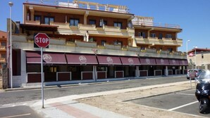 A multi-story building with a stop sign, a row of closed shops with awnings, and a parked motorcycle. - Daluef Alloggi - Loft 1 (Assemini)
