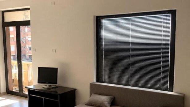 Uma sala de estar moderna com um sofá, uma TV em um suporte e uma janela grande com persianas.