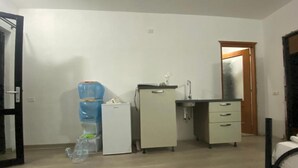 Een kamer met een bed, een kleine keukenhoek, een waterdispenser en een deur.