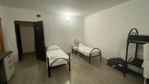 Een kamer met een bed, een ventilator, een stapelbed en een bureau.