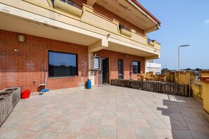 A two-story building with a tiled patio, a large window, and a visible water heater.
