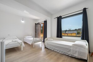 Een kamer met twee bedden, een raam met gordijnen, een plafondlamp en uitzicht op gebouwen.